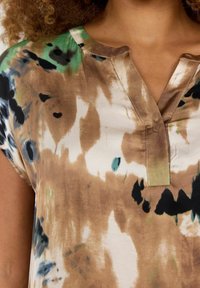 Kurzärmeliges, kragenbewehrtes Oberteil aus leichtem Stoff mit abstraktem Batikmuster in Braun, Grün und Schwarz. Glatte Textur mit dezentem Glanz.