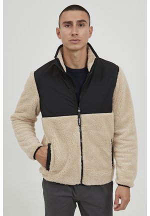 Tan and black fleece jacket with a zip front, sherpa texture on tan sections, and smooth fabric on black chest and sleeves. Features side pockets.