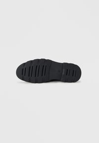Suela de zapato de goma negra con ranuras horizontales, presentando una superficie texturizada y una punta redondeada. Diseño simple sin marcas visibles.