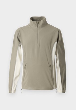 Lett genser i olivengrønn og krem, med høy krage, glidelås, sidelommer, elastiske mansjetter og kontrasterende sidepaneler.