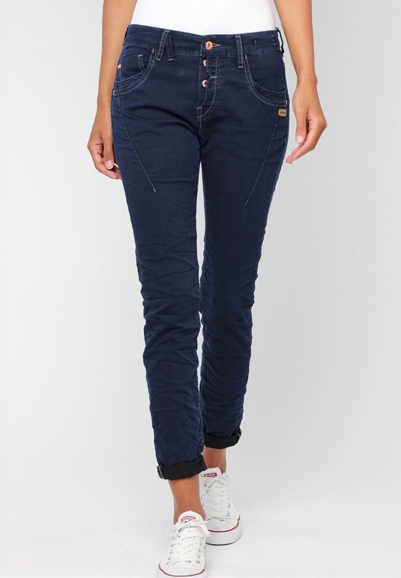 Mörkblå jeans med smal passform, utrustade med knappfäste, sneda framfickor och uppvikta muddar, matchade med vita sneakers.