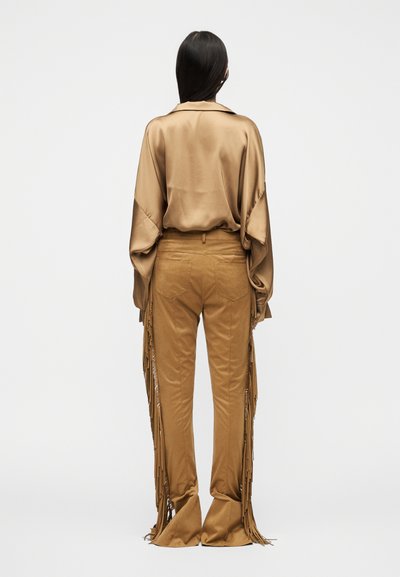 Καφέ σατέν πουκάμισο με μακριά μανίκια και άνετη εφαρμογή, συνδυασμένο με ταμπά παντελόνι που έχει κρόσσια στις πλευρές και φαρδιά τελειώματα.