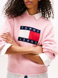 Világos rózsaszín kötött pulóver, mellyel egy tengerészkék, piros és fehér geometrikus logó díszíti a "TOMMY JEANS" felirattal. Bordázott alja és feltűrt ujja van, fehér ing felett viselve.