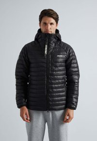 Sort pufferjakke med lynlås i front, høj krave og horisontalt quiltet mønster. Fremstillet af et skinnende, let materiale.