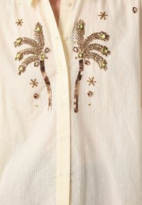 Light cream button-up shirt featuring vertical stripes, embellished with sequin palm trees and crystal accents. Detailed with small star shapes.