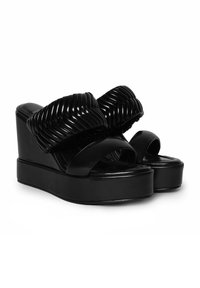 Sandalias de plataforma negras con un acabado brillante, que cuentan con amplias correas trenzadas y un diseño de punta abierta. Suela plana con ligera elevación del tacón.