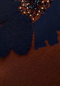 Tissu en maille marron avec application florale texturée bleu foncé et grappes de petites perles dorées et bleu foncé.