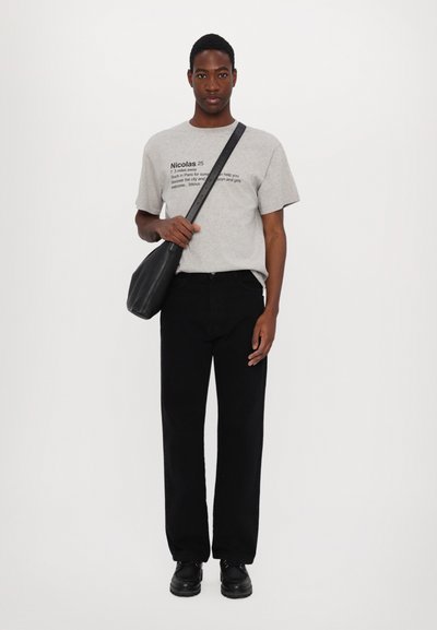 Gray cotton t-shirt with printed text, black straight-leg jeans, and black leather shoes. A black crossbody bag is held in the left hand.