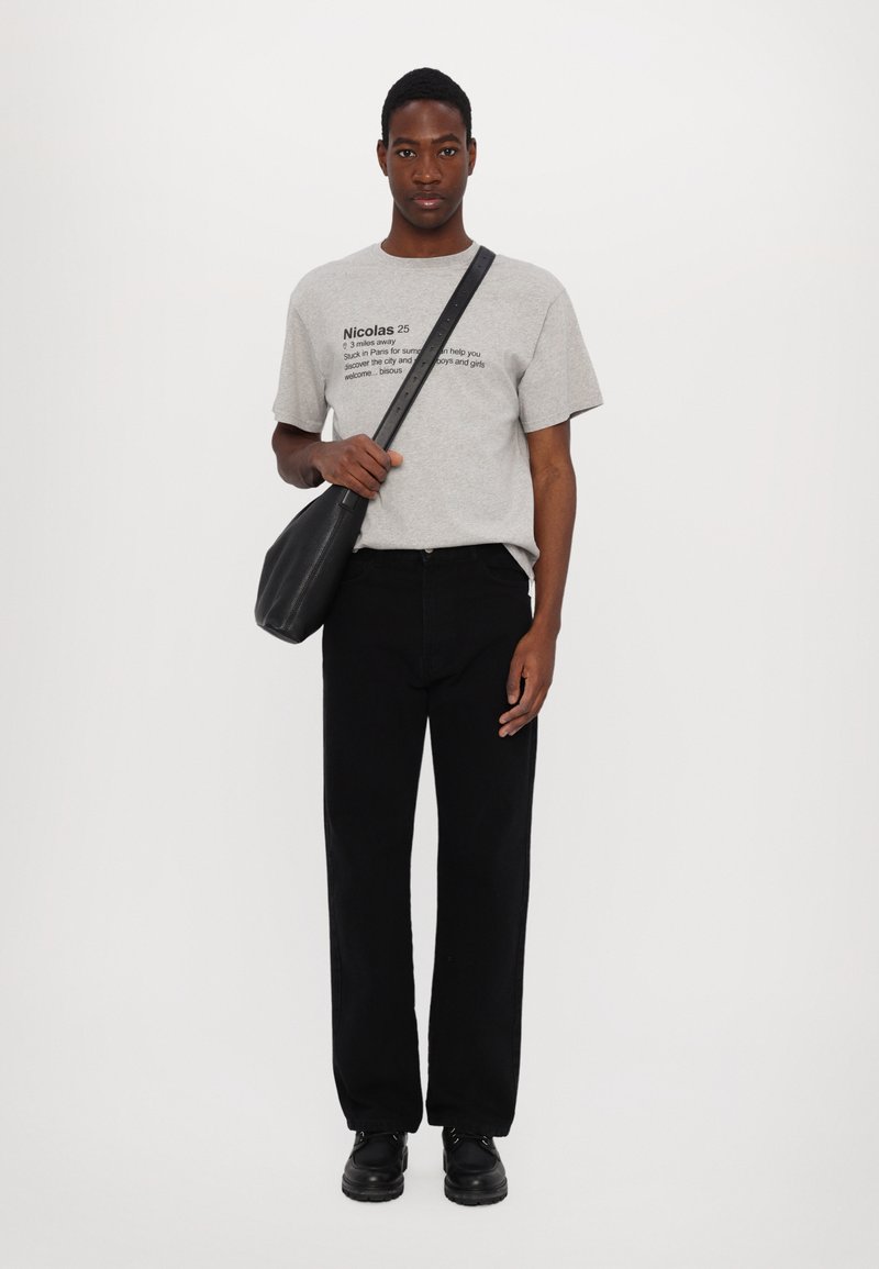 Gray cotton t-shirt with printed text, black straight-leg jeans, and black leather shoes. A black crossbody bag is held in the left hand.