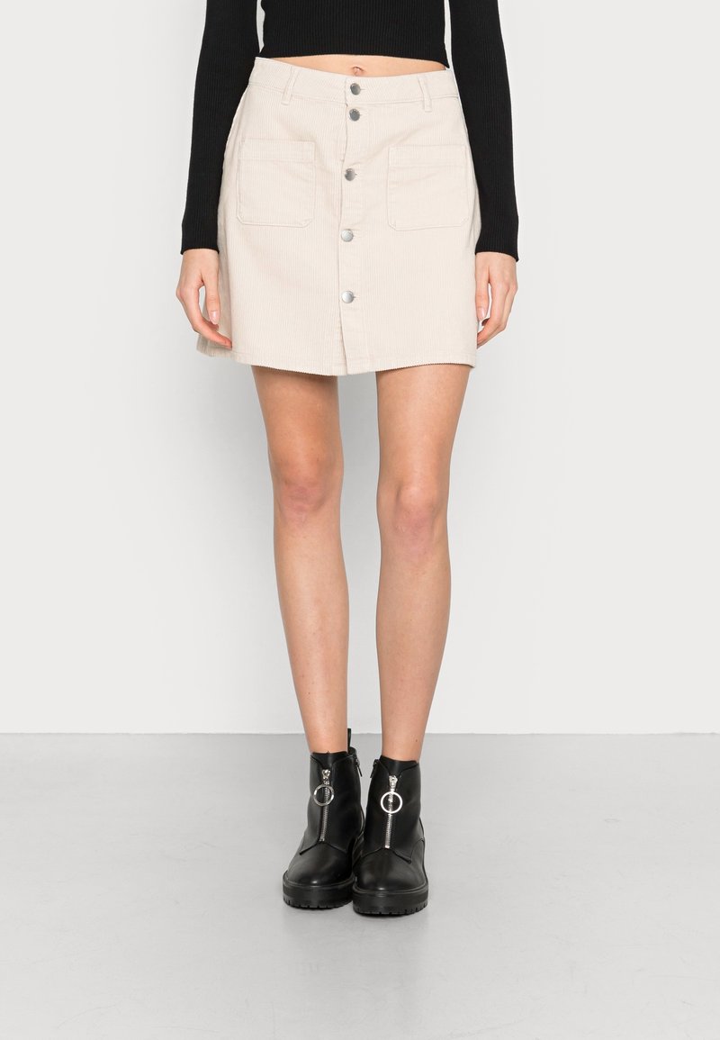 Beige kordkjol med rak skärning, centrerad knappstängning och två fickor fram. Bärs med svarta ankelstövlar med blixtlås.