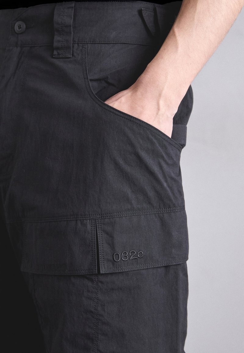 Pantalons noirs à coupe slim, dotés d'une poche latérale et d'un détail de logo surpiqué. Fabriqués dans un tissu léger et texturé.