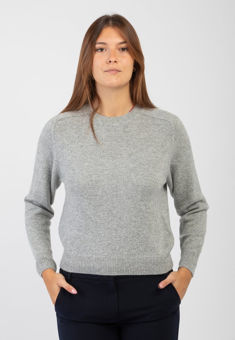 Maglione grigio a maglia con collo rotondo, polsini e orlo a costine, caratterizzato da una finitura testurizzata. Indossato con pantaloni scuri, mani in tasca.