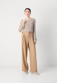 Beige gebreide trui met lange mouwen, gecombineerd met gouden geplisseerde brede broek en beige puntige hakken. Draagt een crème schoudertas.