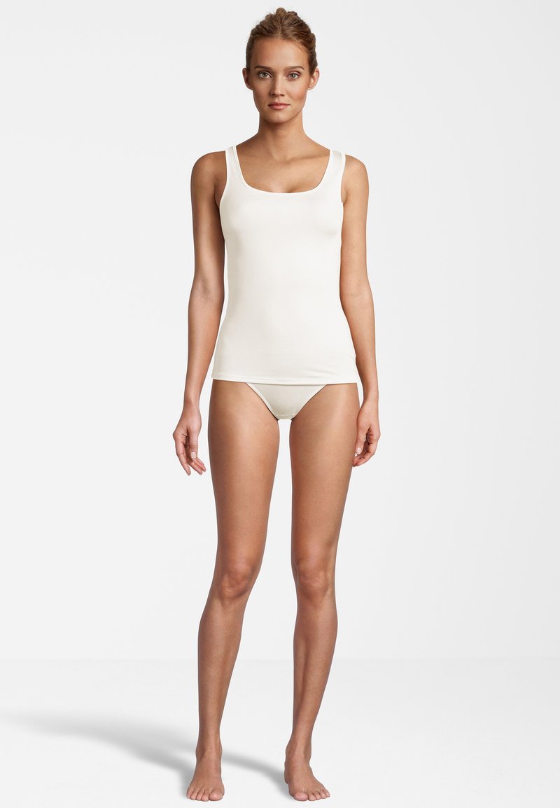 Canotta beige chiaro con bretelle larghe e scollatura a U, abbinata a un bikini senza cuciture in un tessuto liscio e elasticizzato.