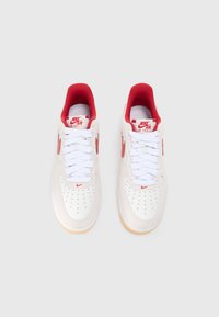 Nike Air Force 1 teniske z belim usnjem, rdečimi poudarki, perforiranim prstom, belimi vezalkami in gumijastim podplatom.