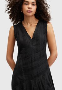 Vestido negro sin mangas con escote en V con ondas, tejido texturizado, acentos de bordado floral y un diseño de falda fluida.