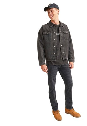 Zwarte spijkerjack met twee borstzakken, gecombineerd met een zwart T-shirt en donkere jeans. Bruine veterschoenen maken de outfit af.