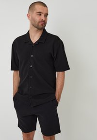 Zwarte korte mouwen overhemd met knopen van een gestructureerde stof en een kraag, gecombineerd met bijpassende zwarte shorts. Eenvoudig ontwerp, ontspannen pasvorm.