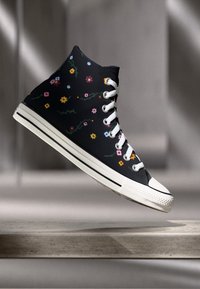 Zwarte high-top sneaker met een bloemenpatroon in verschillende kleuren, witte oogjes en veters, versterkte neus en een gestreepte rubberen zool.