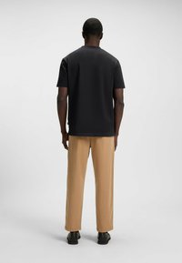 Schwarzes Kurzarm-T-Shirt, lockere Passform, getragen mit beigen Hosen. Glatte Textur, Rundhalsausschnitt, minimalistisches Design ohne sichtbare Logos.