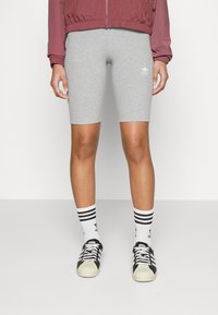 Grå cykelshorts i stretchigt tyg, ihop med svart- och vitrandiga strumpor och svarta Adidas-sneakers. Modellen bär en röd jacka.