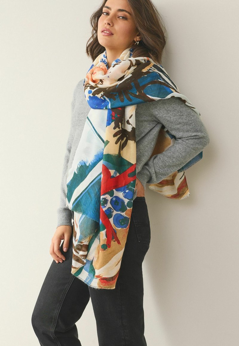 Elav, mitmevärviline sall, millel on abstraktsed lillemustrid, tehtud pehmest kangast, elegantselt pandud halli pluusi peale, lisades tekstuuri ja visuaalset huvi.