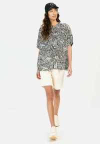 Sort-hvid mønstret top med oversized ærmer, parret med cremede shorts og hvide sneakers. En sort kasket fuldender outfittet.