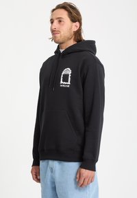 Sweatshirt à capuche noir en mélange de coton, avec une poche avant et un graphisme blanc sur le côté gauche de la poitrine. Coupe standard.