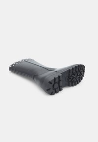 Stivale in pelle nera con suola testurizzata. Caratterizzato da un design decorativo con borchie sulla punta. Costruzione robusta e altezza alla caviglia.