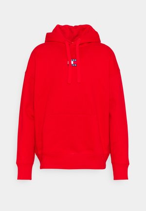 Sweat à capuche rouge en tissu uni, doté d'une poche kangourou à l'avant, d'un cordon de serrage et d'une petite étiquette logo sur la poitrine.