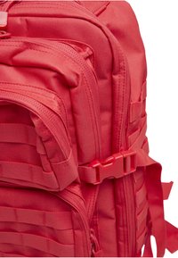 Punainen kangasreppu, jossa on useita lokeroita, vetoketjusomisteita ja säädettävät remmit. Sisältää nauha-aksentteja ja muovisen soljen.