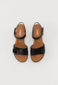 Black leather sandals with adjustable straps and a smooth brown insole. Features a decorative buckle on the front strap.