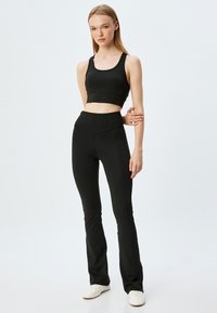 Zwarte sportbeha en high-waisted leggings, beide gemaakt van een gladde stof. De leggings hebben een flared ontwerp en subtiele stiksels.