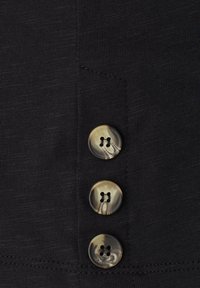 Trois boutons brillants à motif marbré cousus verticalement sur un tissu noir texturé.