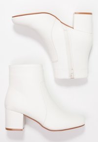 Botas de tobillo blancas con tacones bloque y cremalleras laterales, acabado suave y bordes de suela en color marrón claro, presentadas desde vistas lateral y superior.