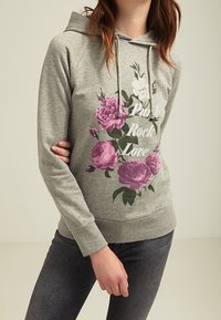 Felpa grigia con un design floreale in rosa e bianco, con la scritta "Rock Love". Tessuto morbido, maniche lunghe e tasca frontale.