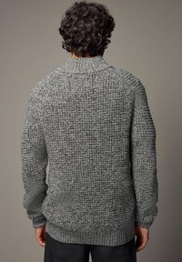 Grå strikket sweater med et tekstureret mønster, ribstrikket krave og manchetter. Designet har en løs pasform og tykk garn for varme.