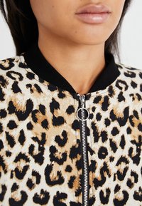 Chaqueta bomber de estampado de leopardo con tejido ligero, cuello negro de canalé y cremallera plateada con tirador circular.