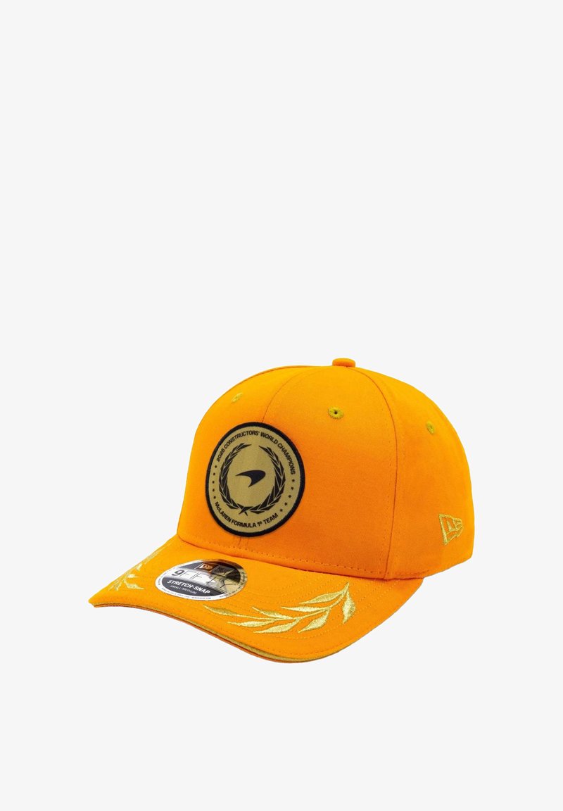 Pomarańczowa czapka z okrągłą czarną naszywką z logo, złotymi haftowanymi akcentami na daszku i usztywnionym fasonem. Posiada płaski rant i regulowany rozmiar.