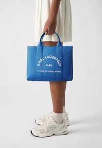 Borsa a tracolla blu con testo stampato bianco "KARL LAGERFELD PARIS 21 RUE ST-GUILLAUME" e due manici robusti, realizzata in materiale testurizzato.