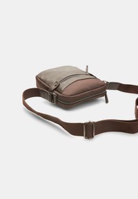 Brown crossbody bag made of synthetic material with a smooth texture, features zipper closure, adjustable strap, and two-tone design.