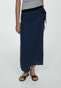 Donkerblauwe denim wikkelskirt met een strik in de taille, een enkel lengte ontwerp en een zachte textuur, gecombineerd met bruine sandalen.