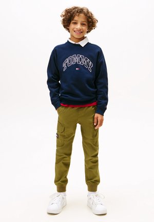 Sweatshirt bleu marine avec l'imprimé "TOMMY", col blanc, pantalon cargo olive avec poches et baskets blanches à lacets. Tenue décontractée pour enfants.