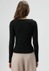 Zwart geribd topje met lange mouwen, brede halslijn, aansluitend model en lichte uitlopende taille, gecombineerd met lichtbeige, op maat gemaakte broek.