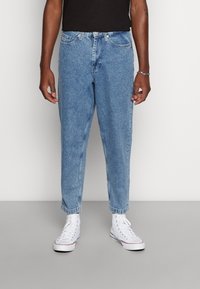 Ljusblå denimjeans med tapered fit, som har fem fickor och uppvikta nederdelar, kombinerade med vita hightop sneakers.