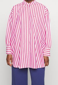 Camisa de manga larga de botones en rayas verticales rosas y blancas, con un cuello puntiagudo y un bolsillo en el pecho, fabricada en tela de algodón.