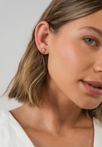 Goldene Schildkröten-Ohrstecker mit filigranen Details, die eine strukturierte Oberfläche aufweisen und klein sind, getragen an dem Ohr eines Modells.