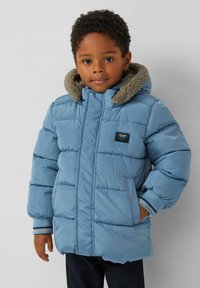 Gevoerde blauwe jas met een donzige capuchonvoering, geribbelde manchetten met blauw-witte strepen, en een borstlabel aan de linkerkant.