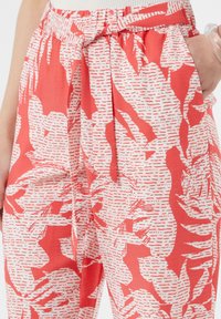 Rot-weiße gemusterte Hosen mit einem Kordelzugbund, die Palmblatt-Designs und strukturierten Stoff aufweisen. Zwei Seitentaschen sind sichtbar.