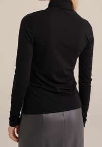 Svart långärmad polotröja i mjukt tyg, med en figurnära design, slät textur och minimalistisk stil.